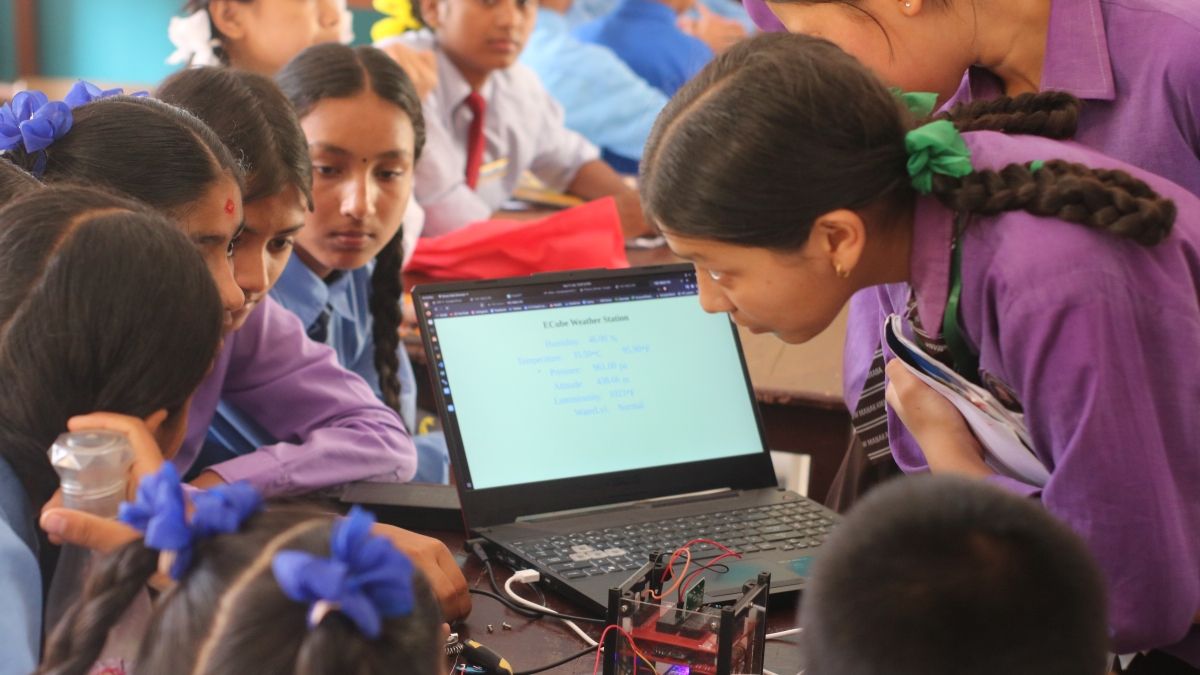 A group of Nepalese girls in school uniforms sitting around a laptop with a robotics kit.