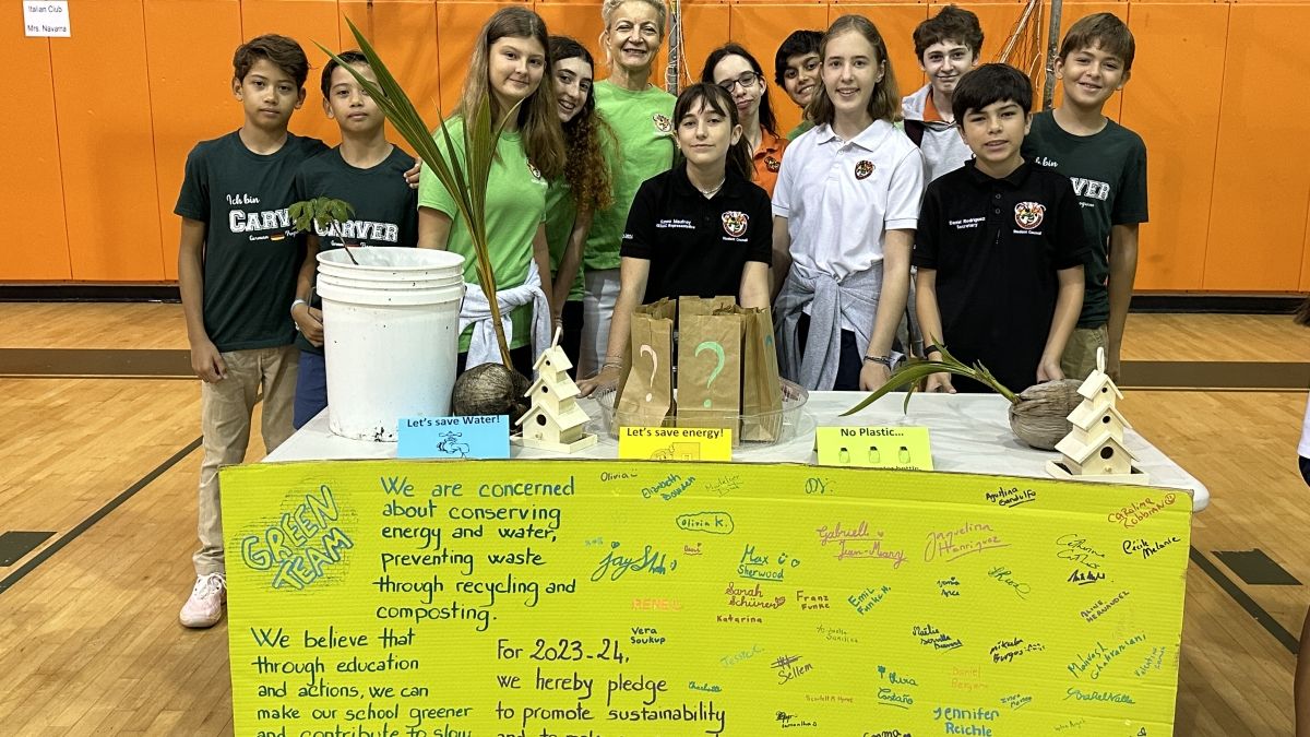 A group of young students in a gym standing behind a table decorated with posterboard that says Green Team