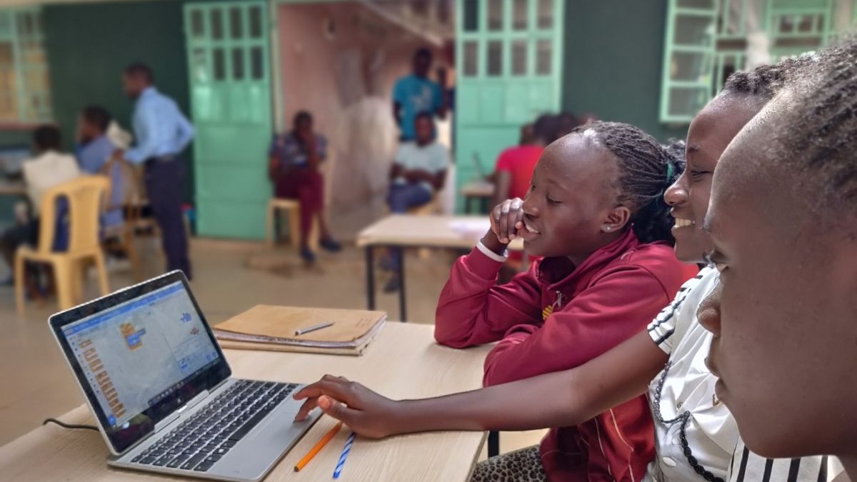 Three Kenyan girls sitting at a desk at school infront of a laptop