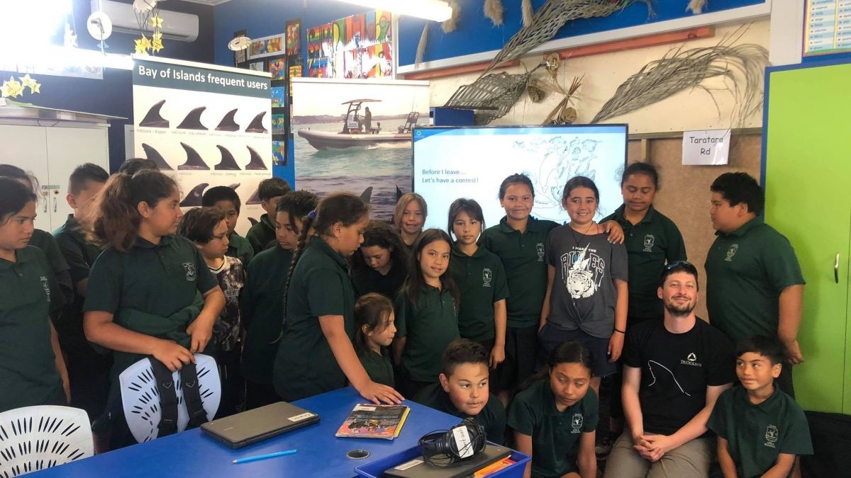 A group of middle school children posing together in a classroom, in front of a poster of shark fins