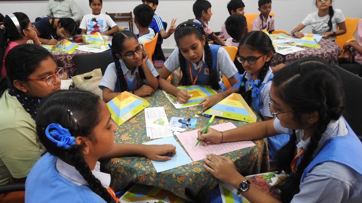 Six girls in school uniforms sitting around a table with colorful pyramid-shaped diagrams.