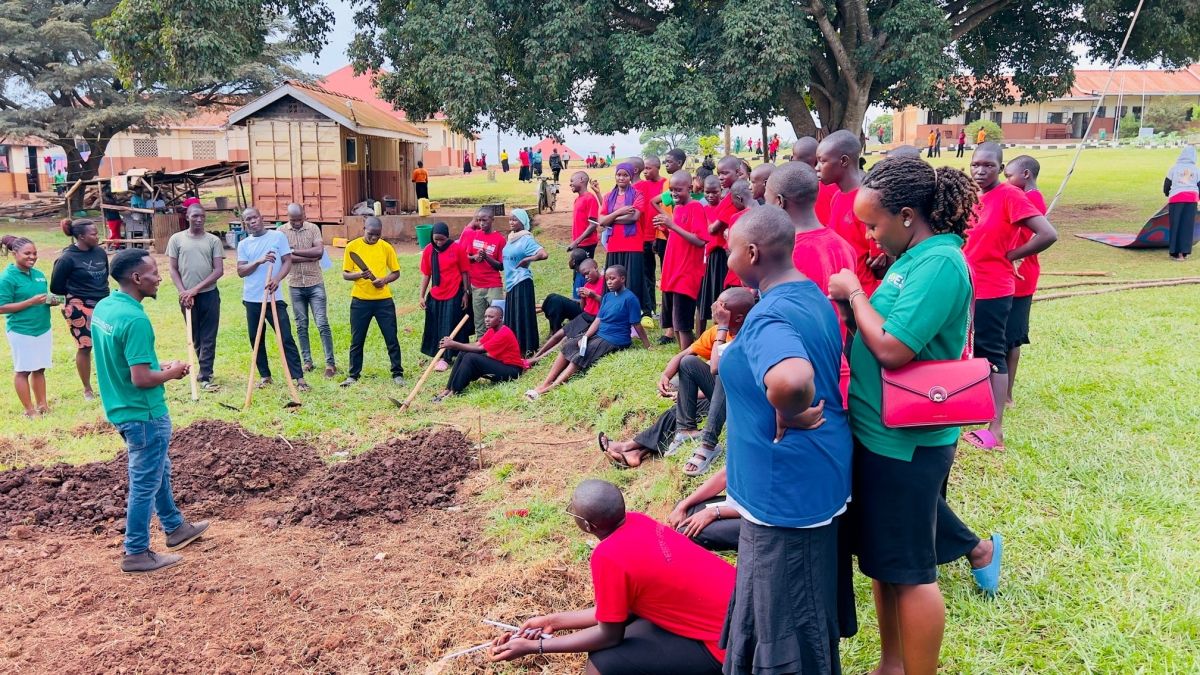 A group of students and teachers outside standing with garden hoes around several holes dug for plants