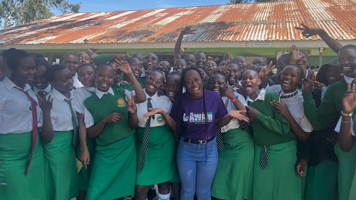 A group of teenage girls posing for a group photo in front of their school, smiling and waving their arms