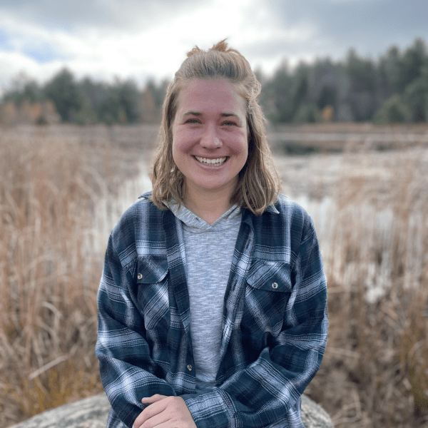 A person smiling sitting on a boulder in the middle of a field