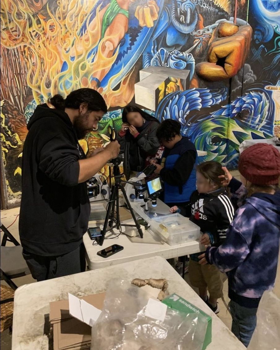 Jiapsi sharing microscope equipment and offering a mushroom cultivation workshop for youth during the POC Fungi Community’s “Siembra comida, arte, conciencia” event in 2022 at a local community art and cultural center.
