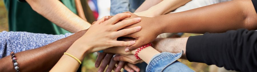 Diverse set of hands all stacked on top of one another in outdoor group huddle.