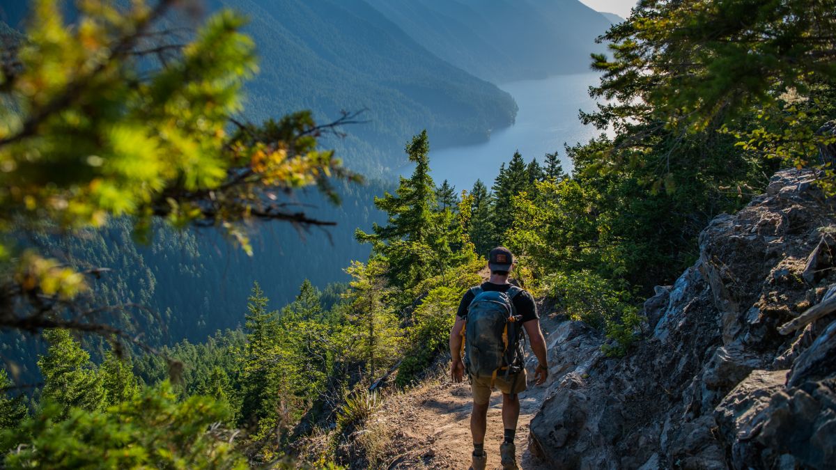 person hiking a mountain trail overlooking a lake