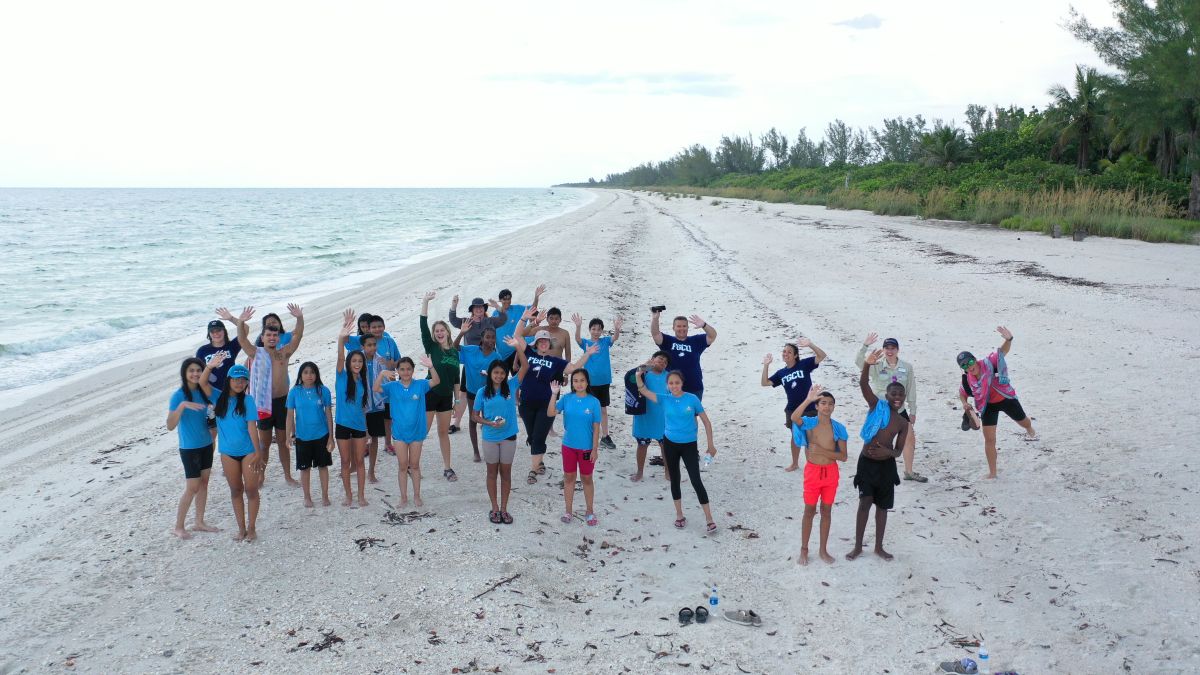 a group of students in blue t-shirts posing for a photo on a beach
