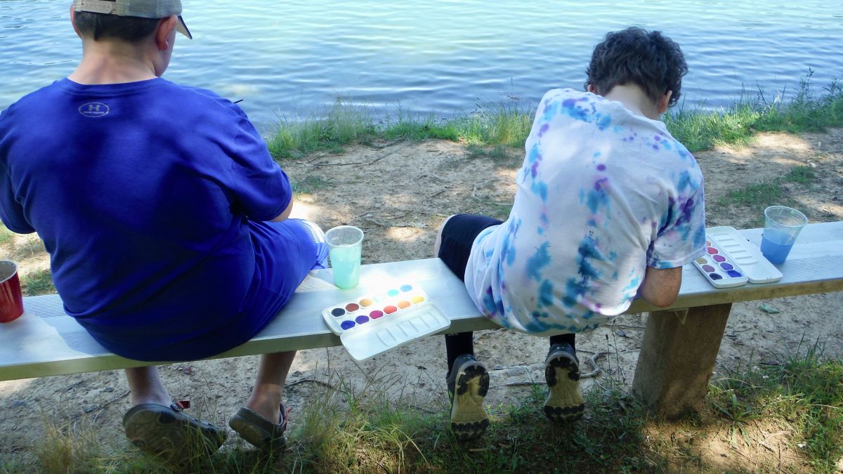 Two students sit outside painting. 