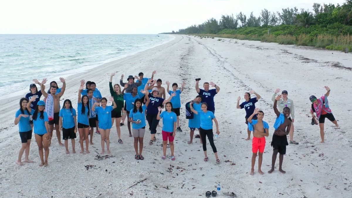 Group of people on a beach wave at the camera