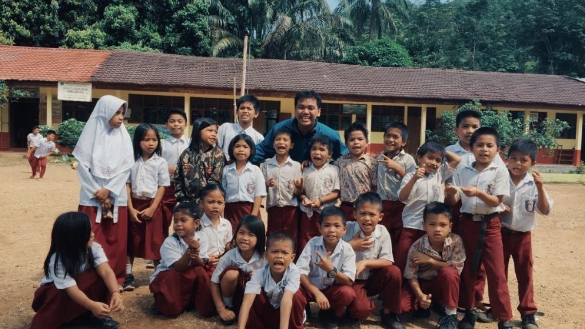 A young leader surrounded by students posing for a group photo