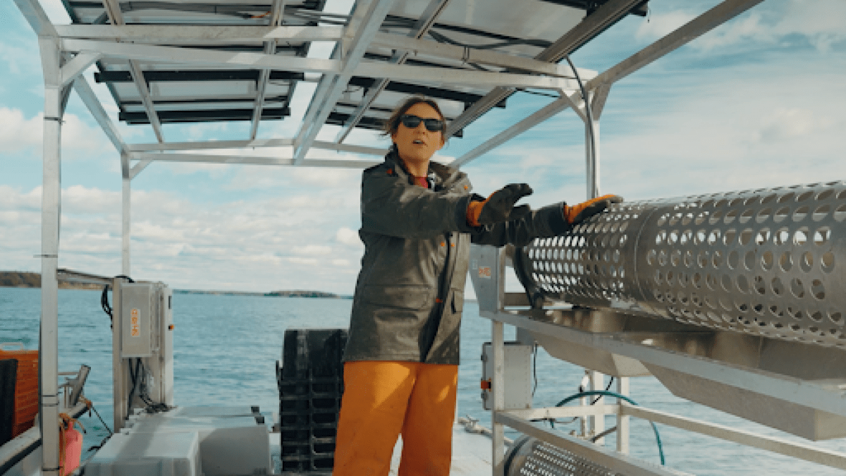 A woman in rubber rain gear steers a barge on the ocean