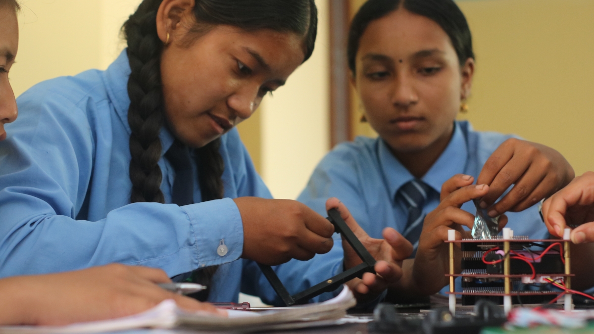 Two girl students in uniforms working on a STEM kit
