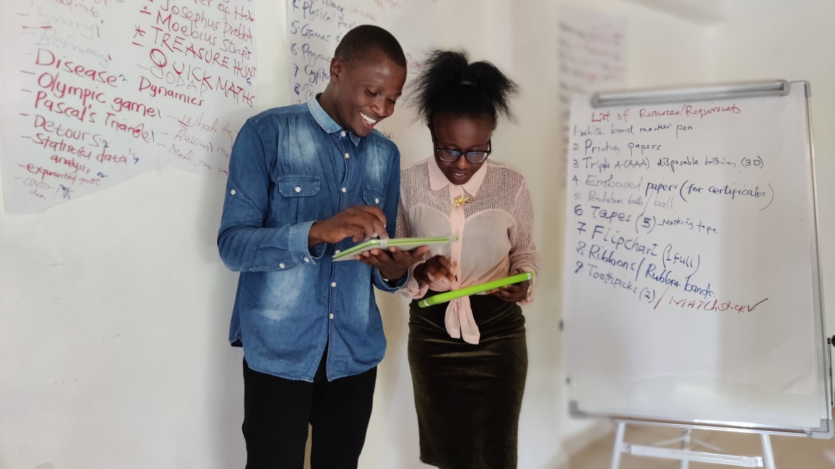 A young man and woman looking at tablets standing in front of white boards full of text