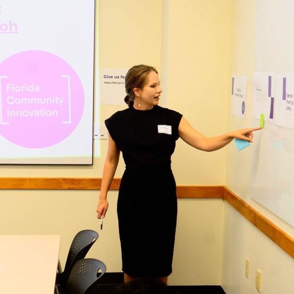 Caroline Nickerson in a black dress pointing at a whiteboard