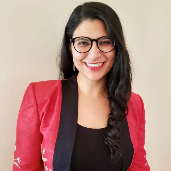 A person smiling with long black hair wearing glasses and a red jacket