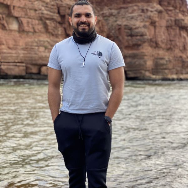 A person smiling and standing in water with a rock face in the background containing red hues