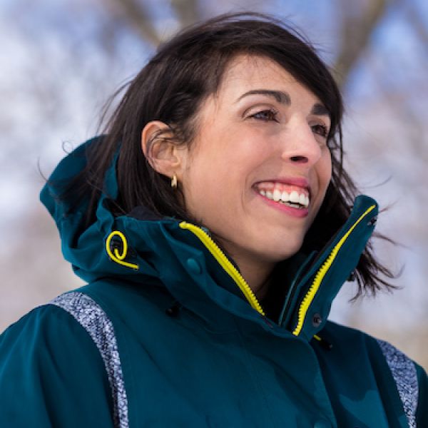 A Person Smiling In A Blue Jacket With Yellow Trim On A Winter Day