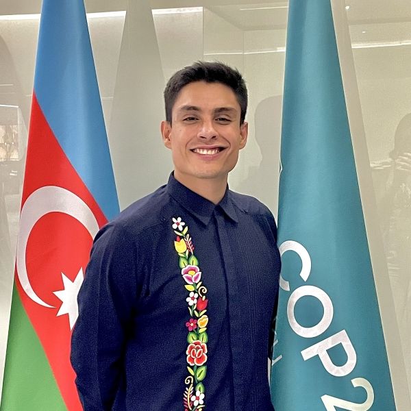 Man in blue shirt standing smiling in front of two flags