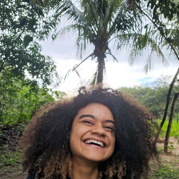 A woman smiling outdoors under trees