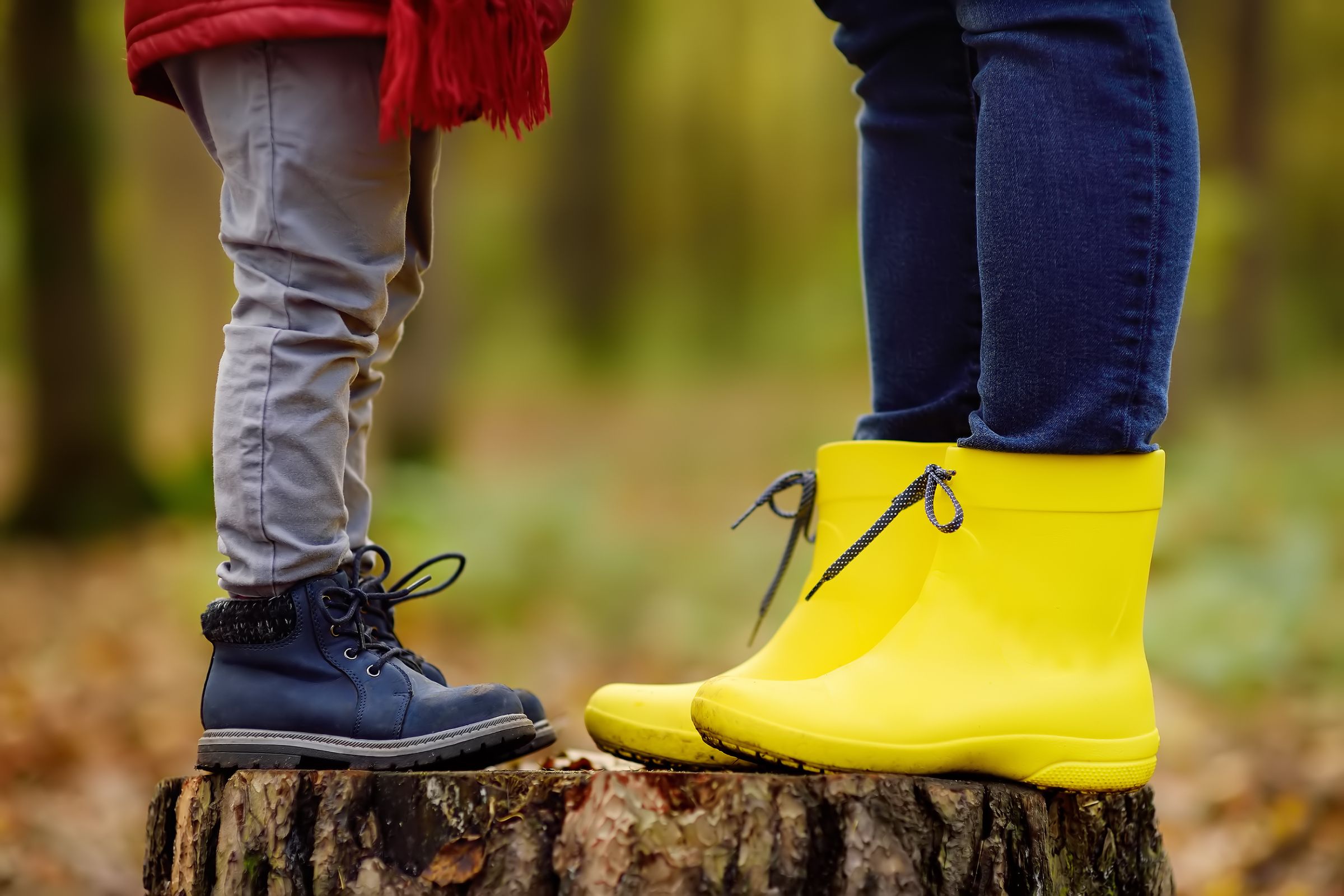child and adult in boots standing on tree stump