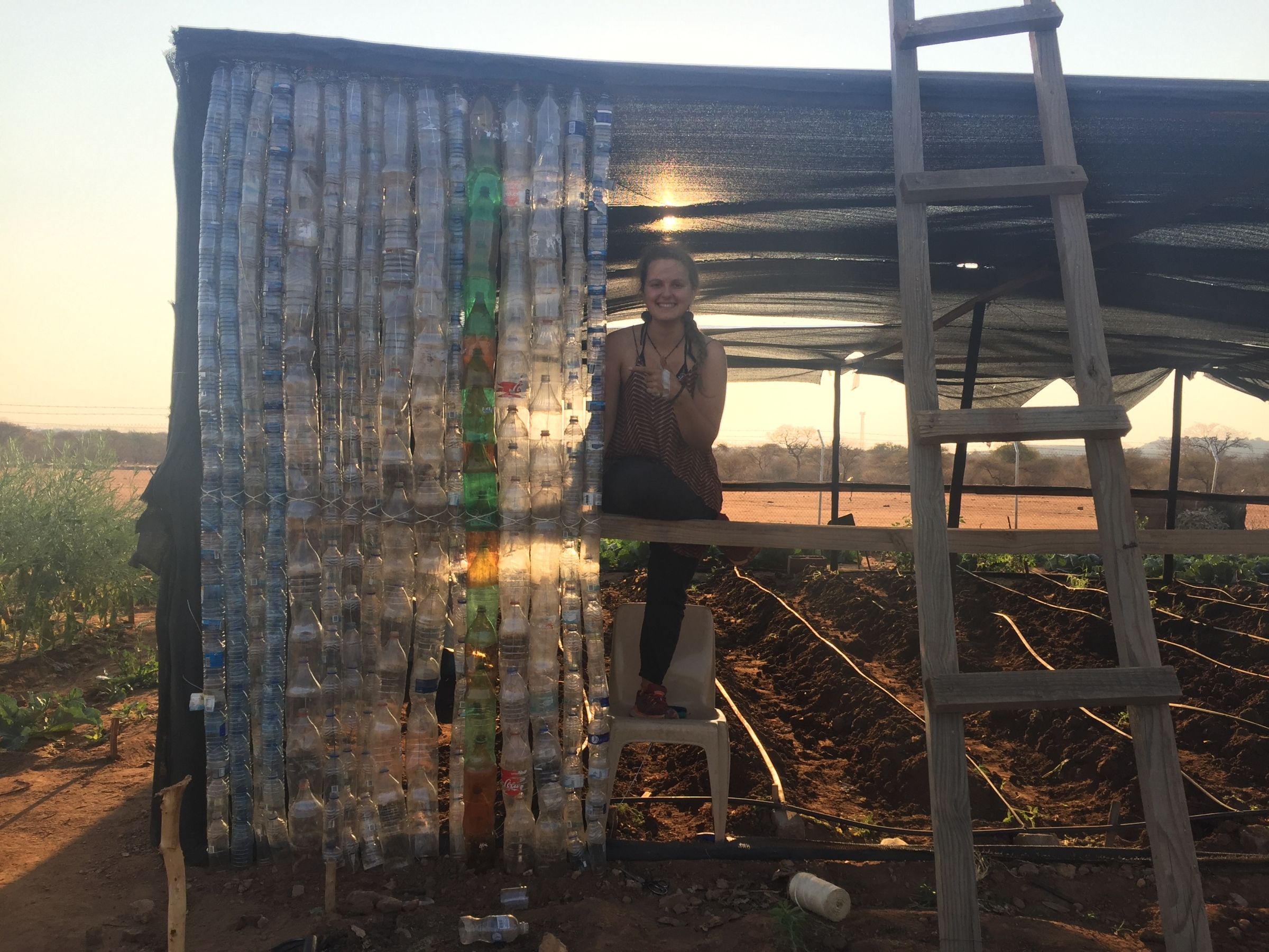 Katka next to a community upcycling project - waterbottle greenhouse from trash collected in nearby bush, in Botswana.