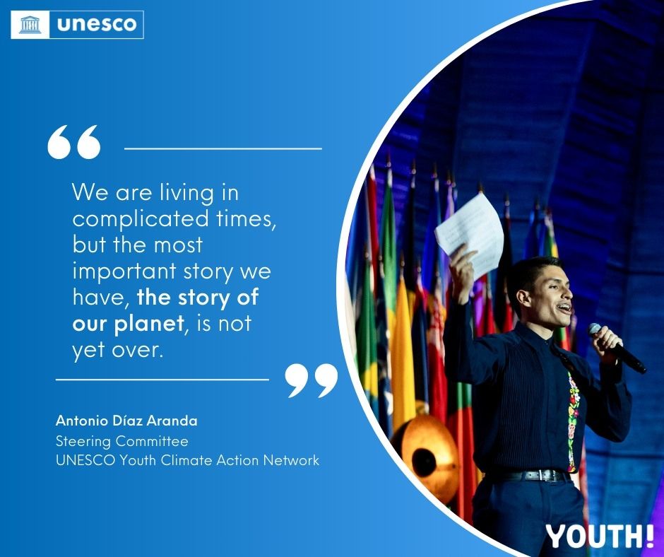 Young man speaking on a stage with flags, with a quote