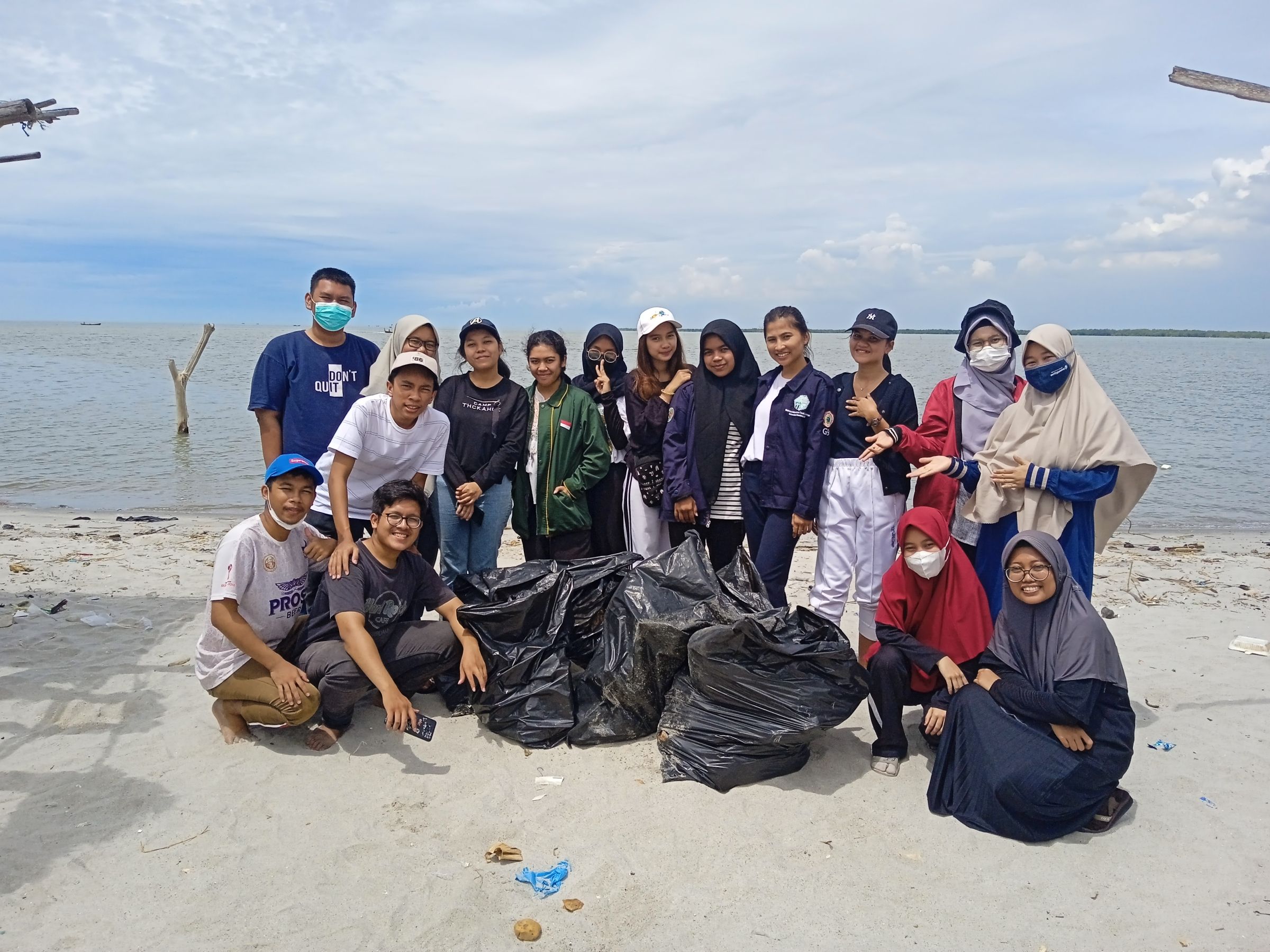 A group of young people on the beach with bags of pick-up trash.