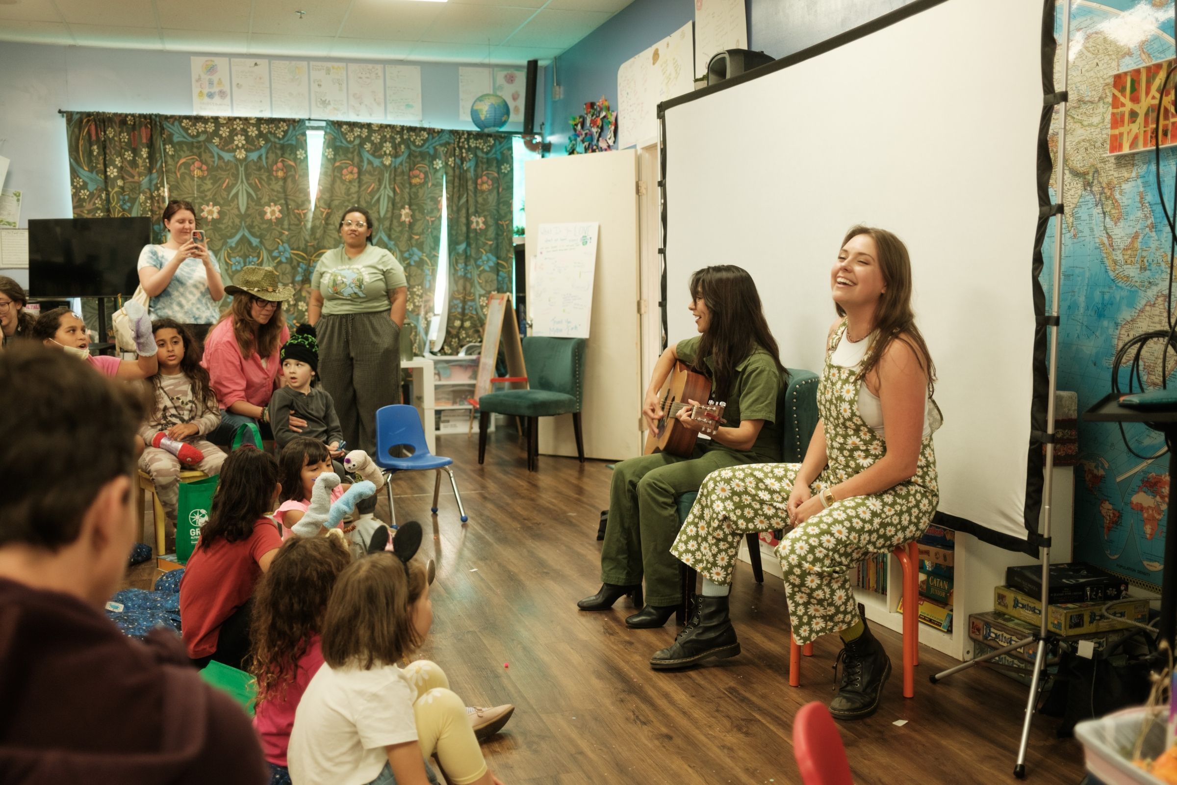 Two performers, one with a guitar, in front of a group of children.