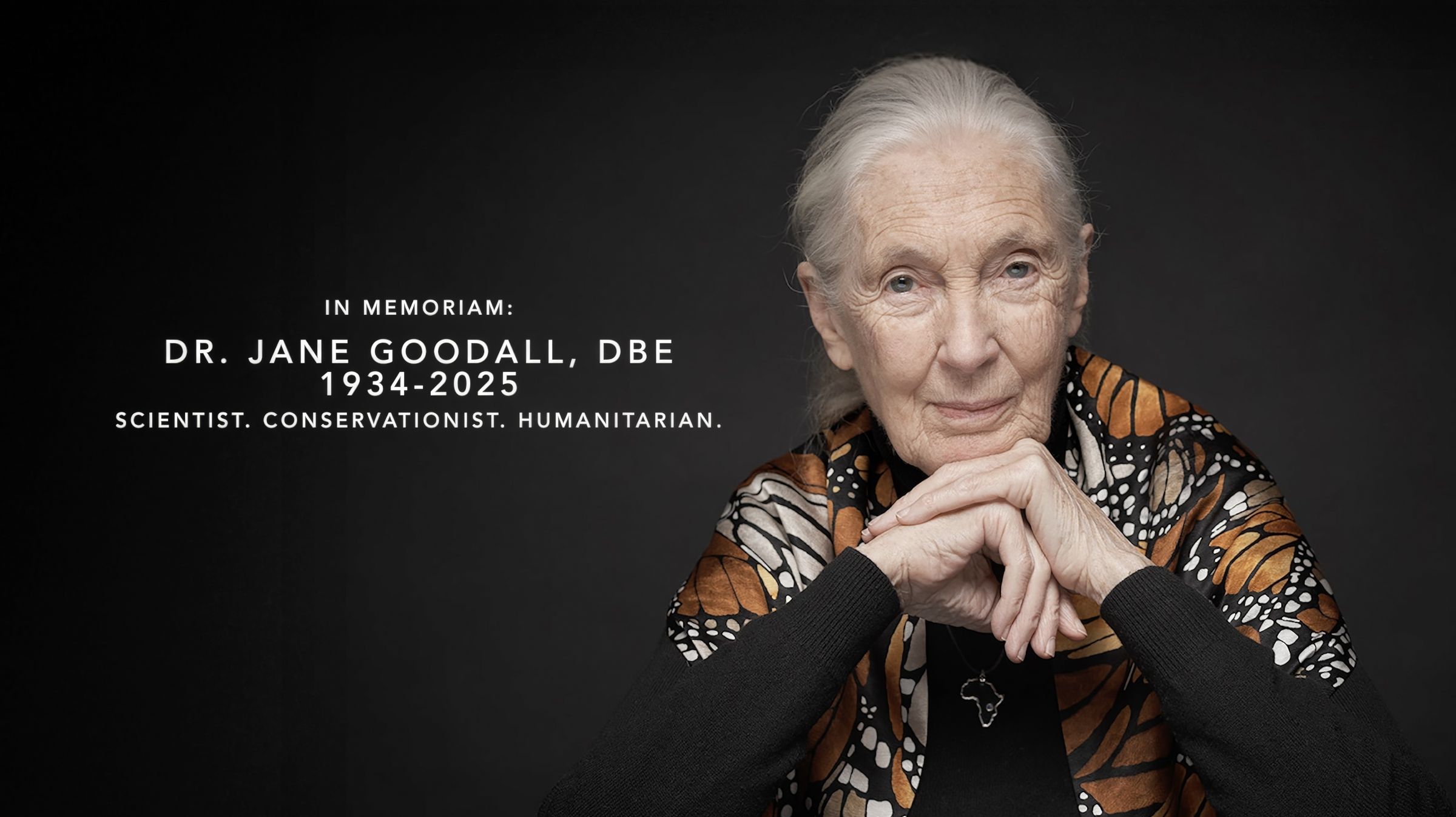 Jane Goodall gently smiles, wearing a monarch butterfly-printed shawl, next to the words, "Dr. Jane Goodall 1934–2025"