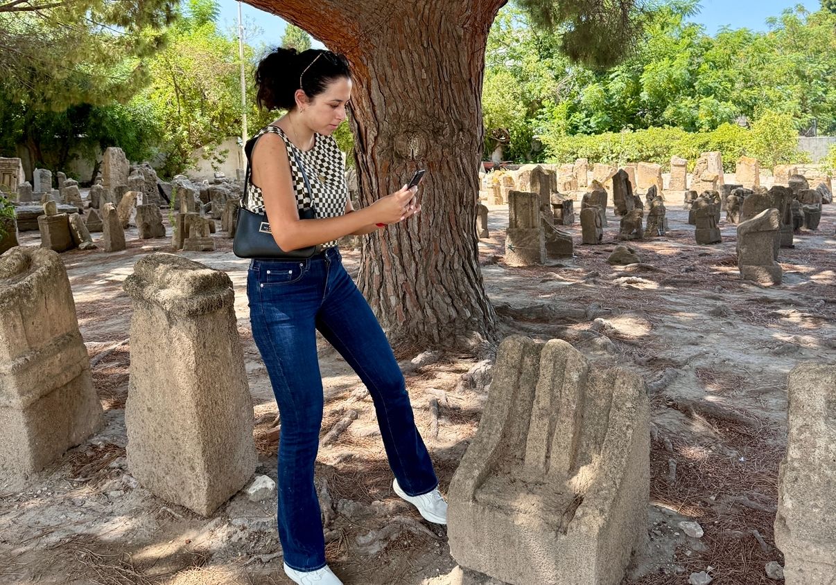 A woman outside holding a smartphone over ruins