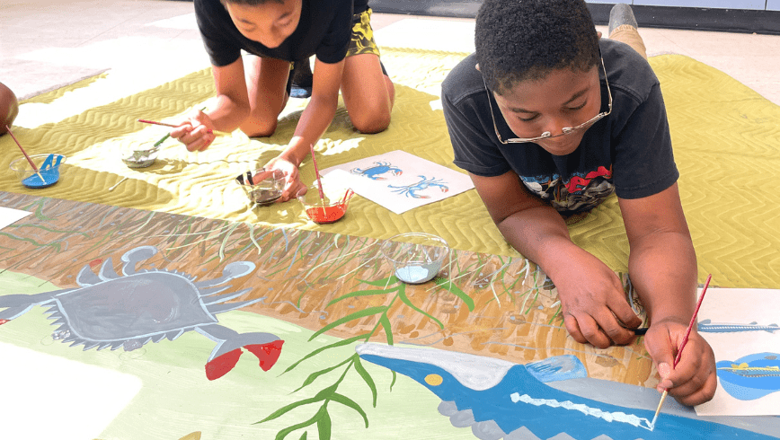 Two students paint a watershed scene in a mural