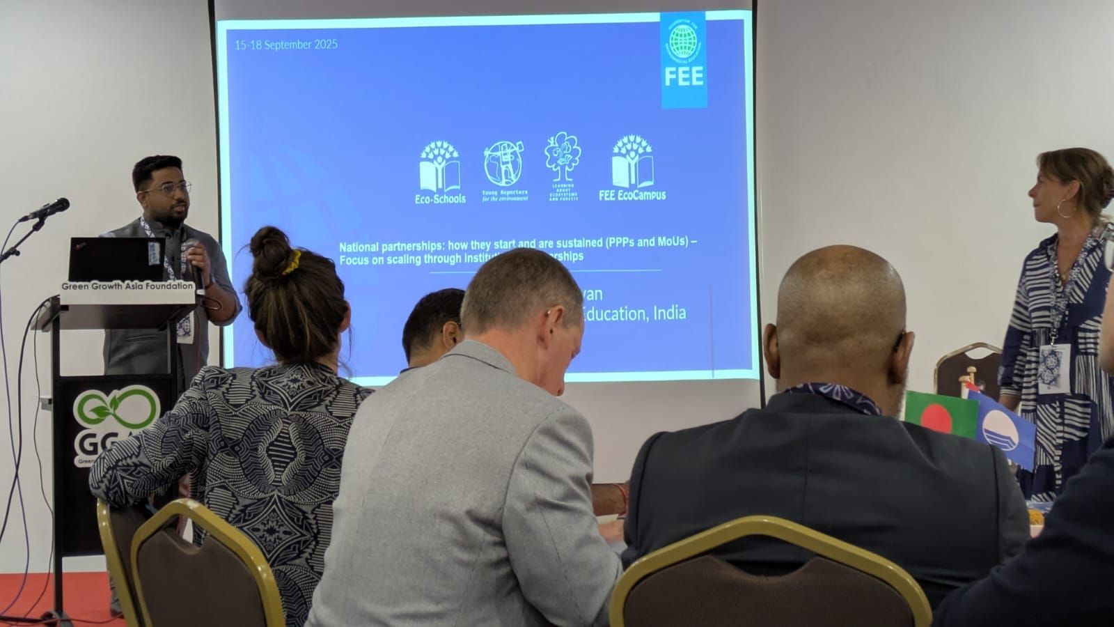 A person standing and speaking in front of a group of seated people.