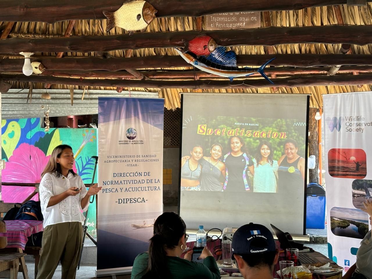 A person stands in front of a presentation board and banner, text reads "Direccion De Normatividad De La Pesca y Acuicultura, Dipesca, Socializacion"